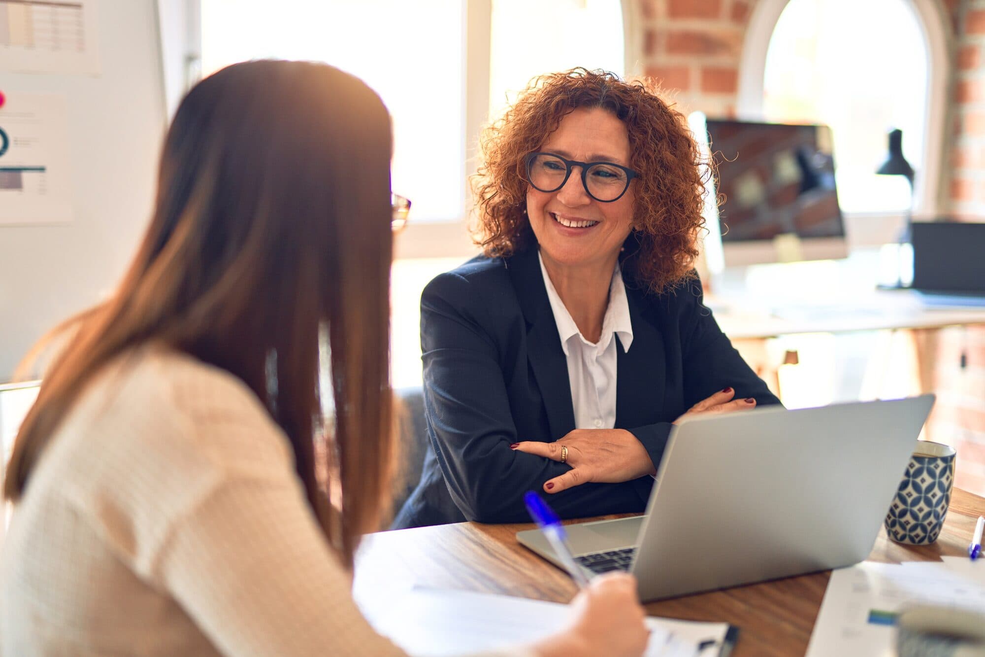 A leader talks through a plan with a colleague at her laptop