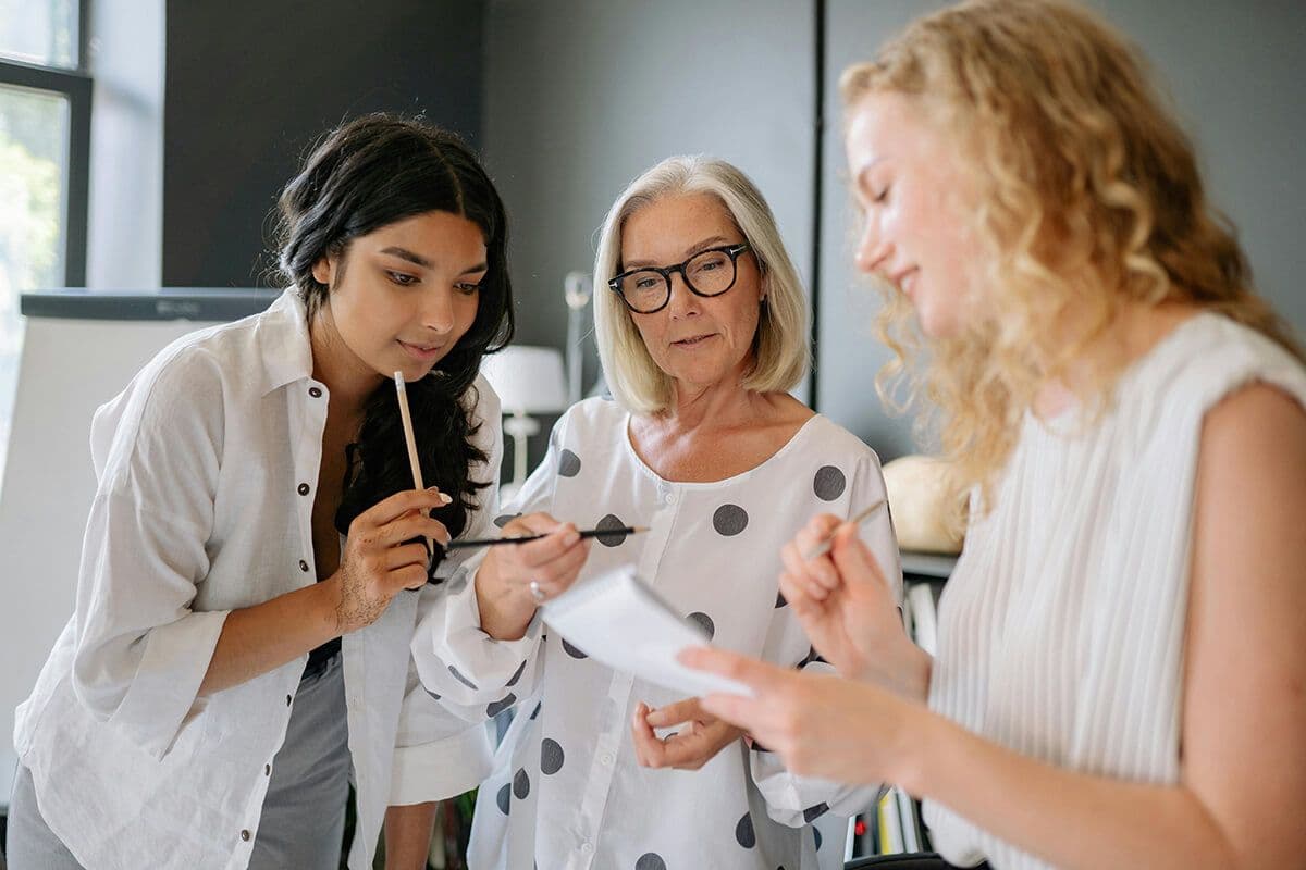 Two young women meet with an older woman in the office as part of a team mentoring program at their company