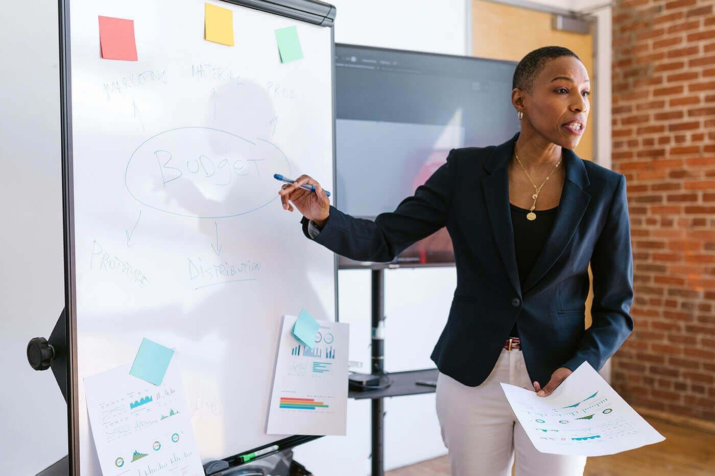 A woman presents ideas at a whiteboard covered in sticky notes