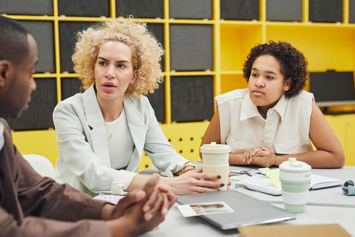 Woman sitting with two colleagues in yellow conference room discussing culture at the company.