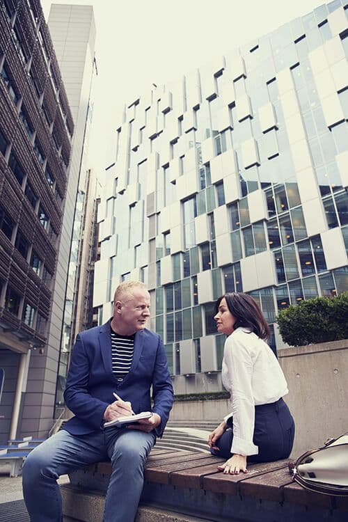 Manager taking notes during a one-on-one conversation with an employee outdoors