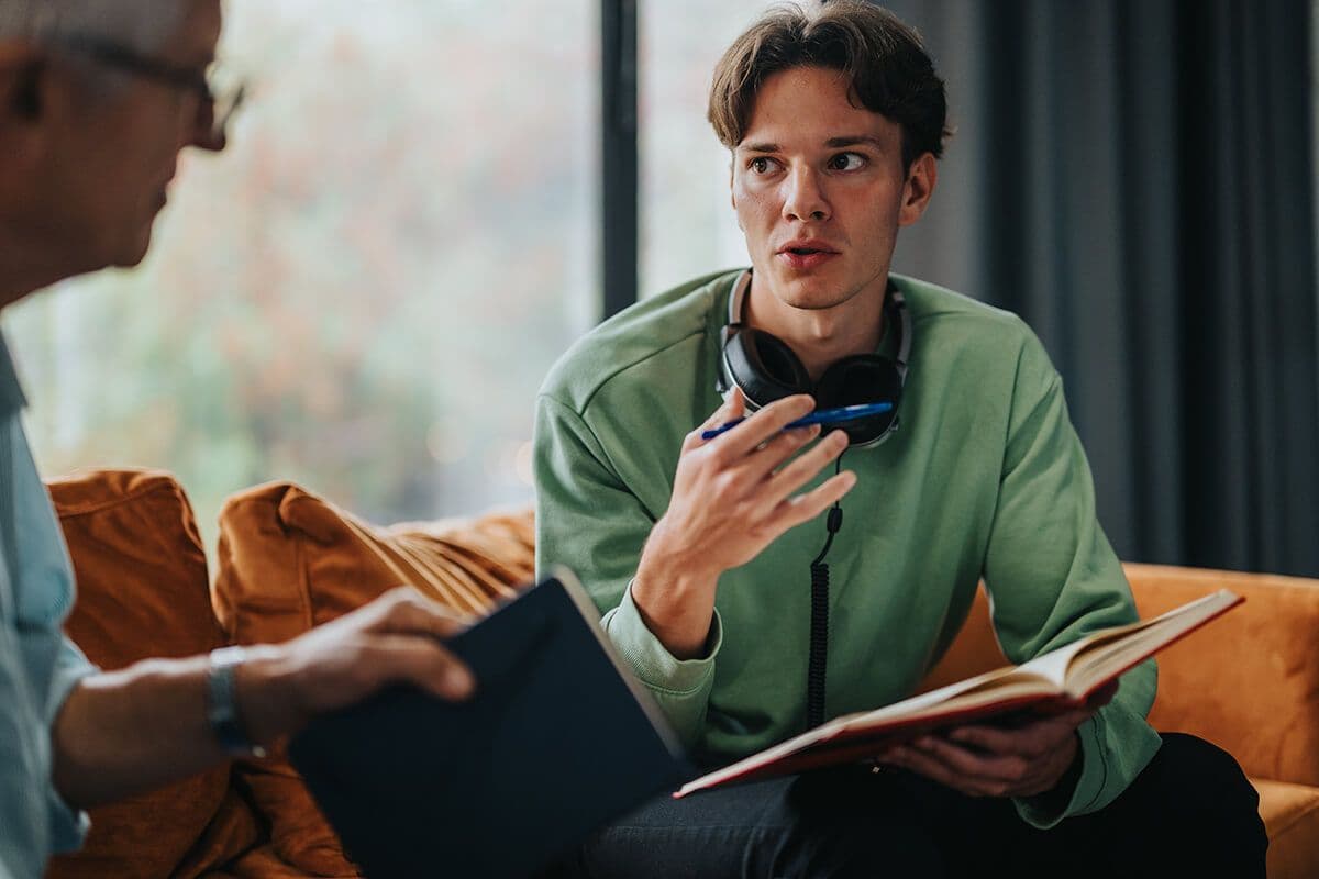 Man sitting on a couch with headphones on in an office talking to his mentor about AI in mentoring and coaching