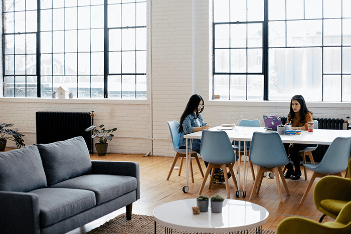 two women working at a table on laptops in an open loft office