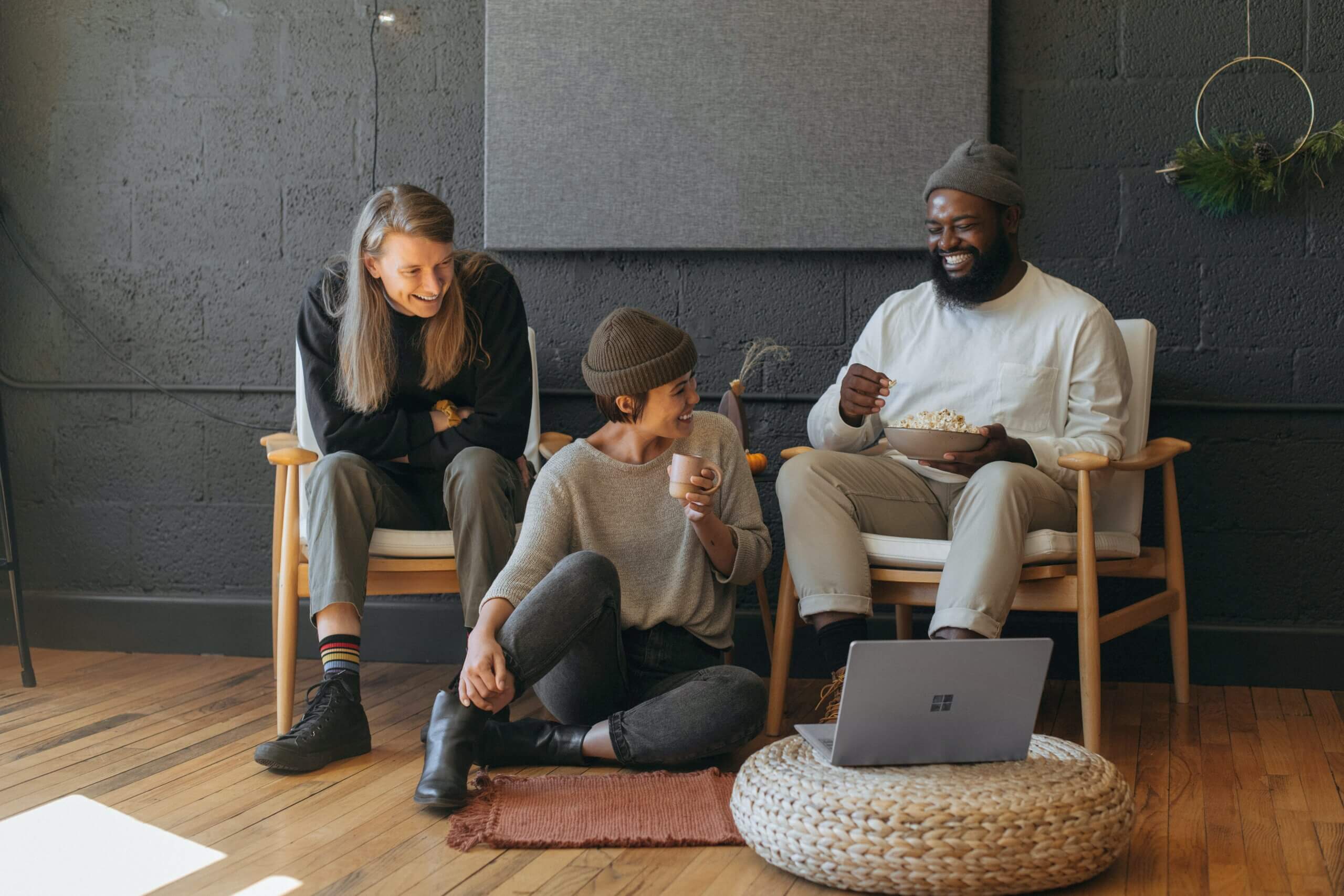 three employees sit in an office drinking coffee and eating popcorn during mentoring session
