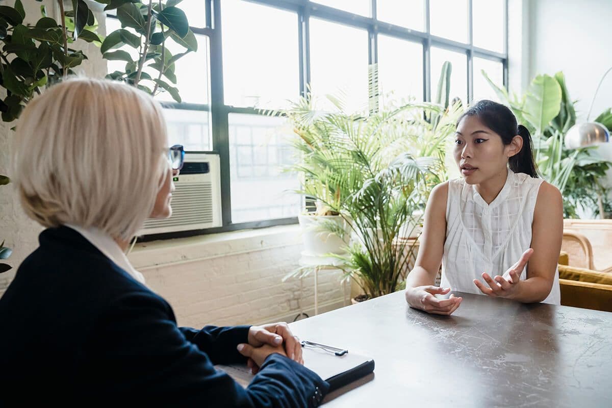 Two women employees sitting at a desk in an office arguing about mentoring challenges